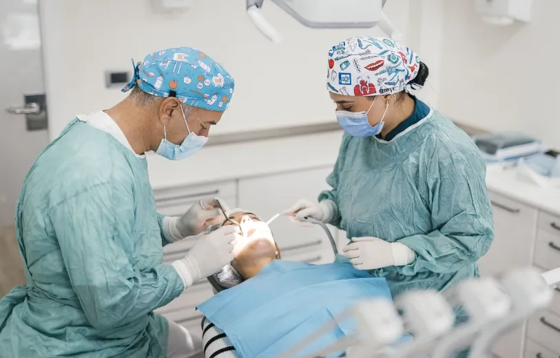 Dos profesionales de la Clínica Dental Moaña con bata y gorro quirúrgico realizando una intervención a un paciente